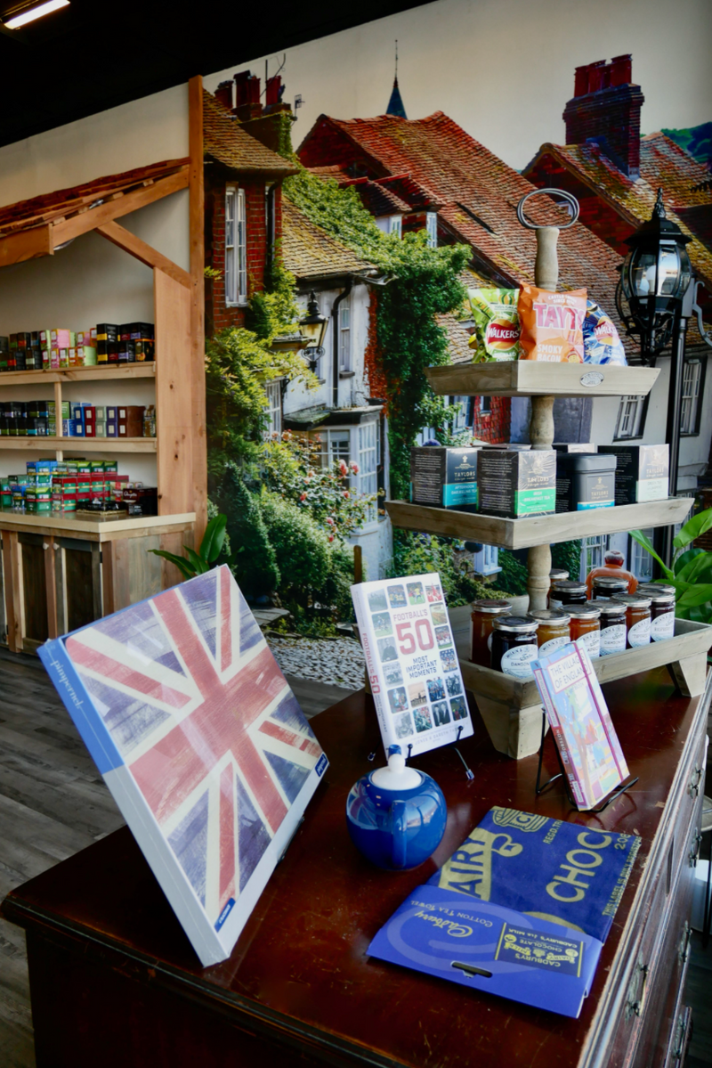 Interior display table at The Hamlet British store showcasing British‑themed merchandise in front of a mural of a quaint English village